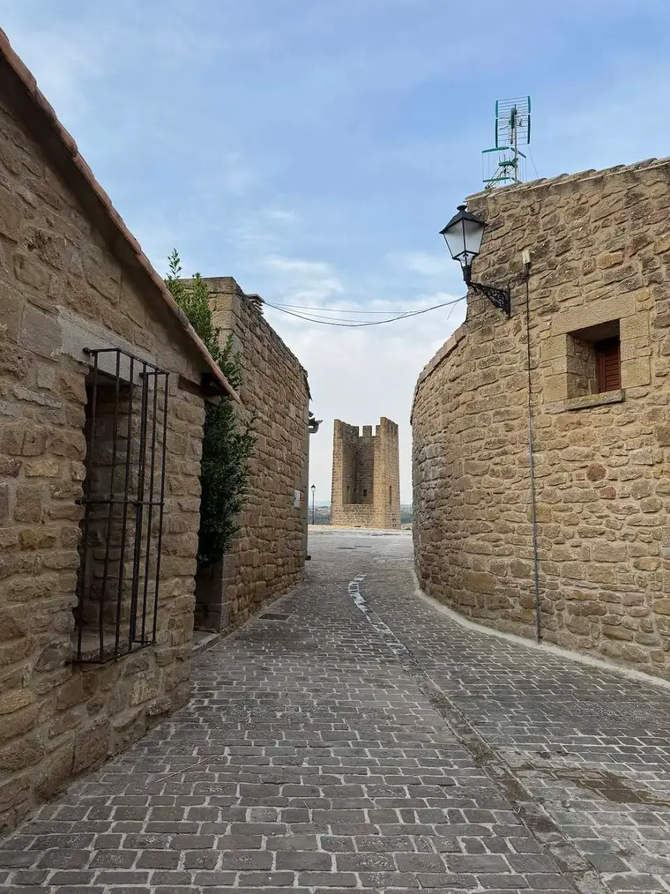 Calle empedrada entre casas de piedra con un torreón al fondo