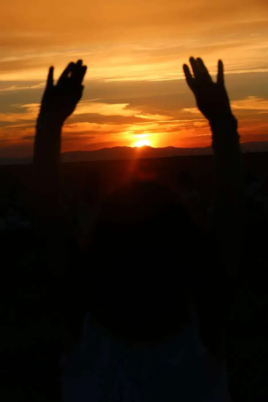 Manos al cielo frente a la puesta de sol