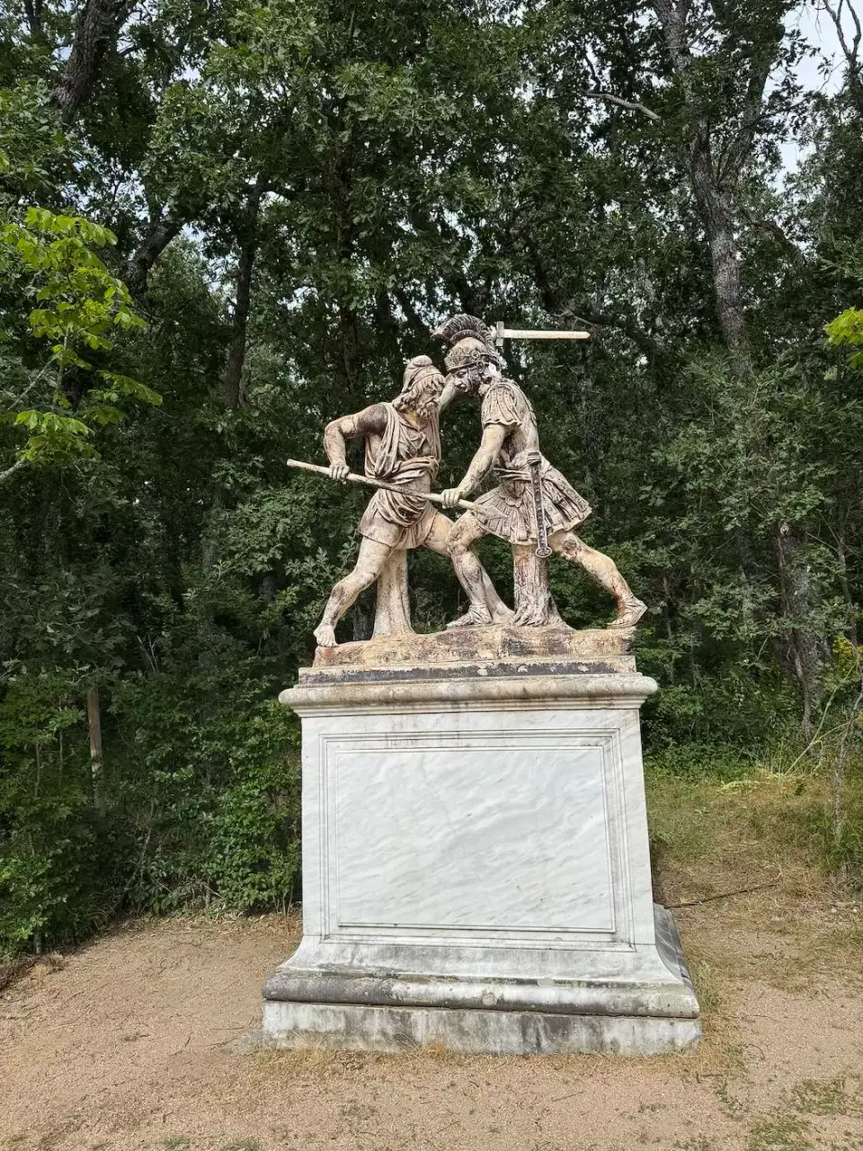 Escultura de dos figuras luchando sobre un pedestal blanco