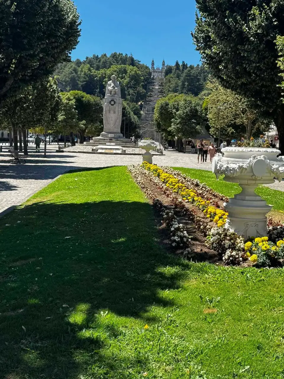 Jardín con césped, flores y una estatua bajo cielo azul