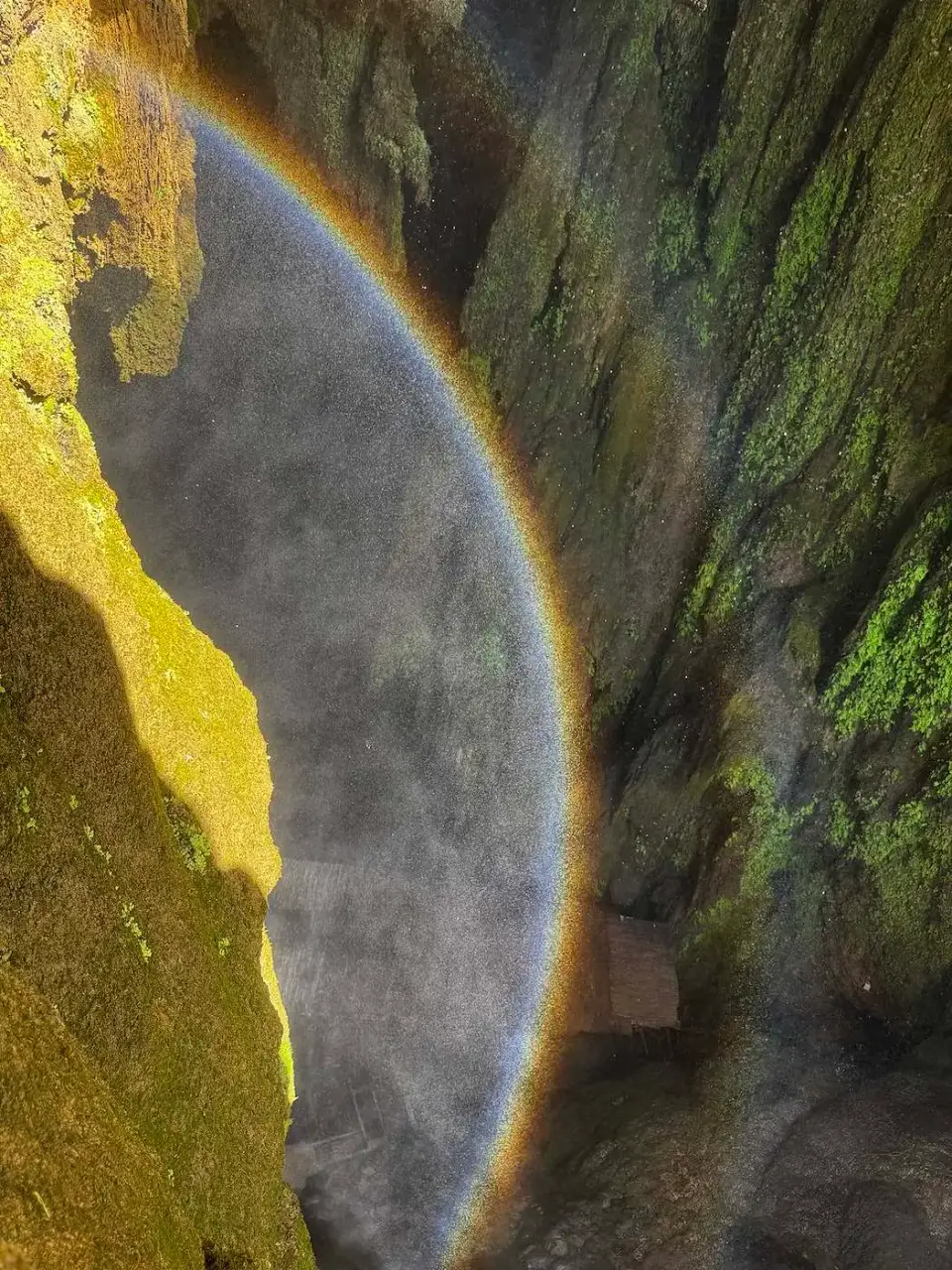 Arcoíris en la bruma de una cascada entre rocas con musgo
