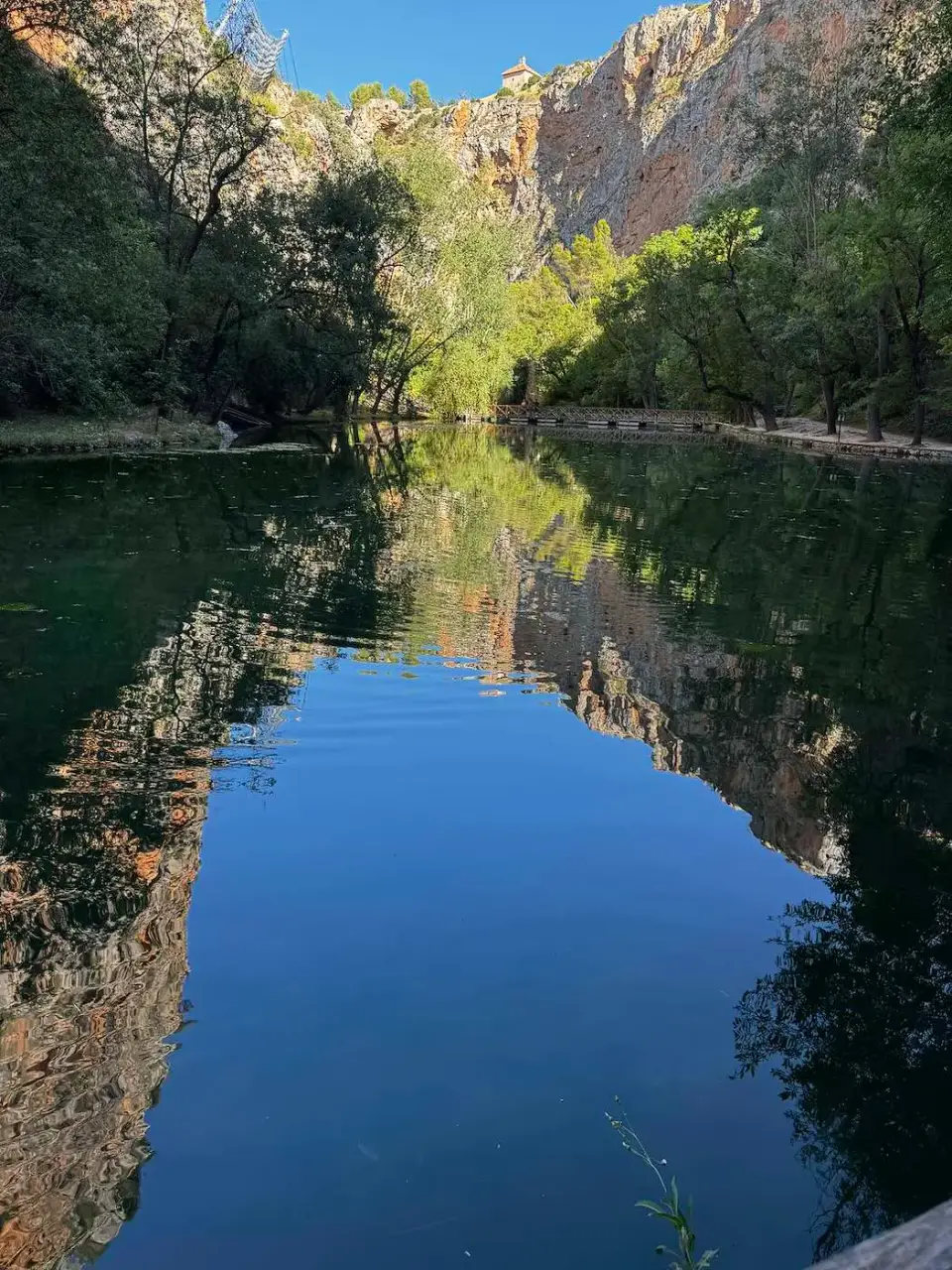 Lago de aguas quietas que refleja los acantilados y árboles