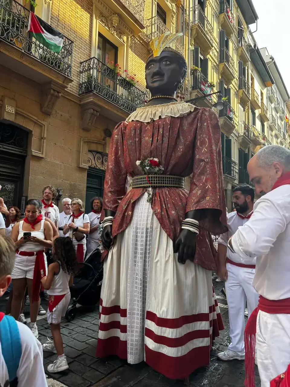 Gigante de la comparsa desfilando entre gente vestida de blanco y rojo