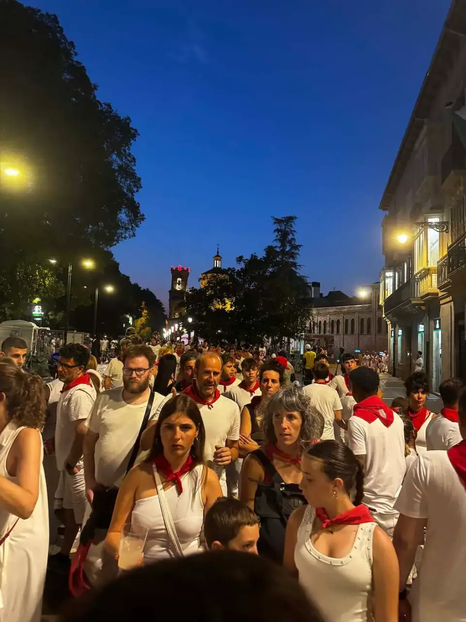 Multitud vestida de blanco y rojo en las calles al anochecer