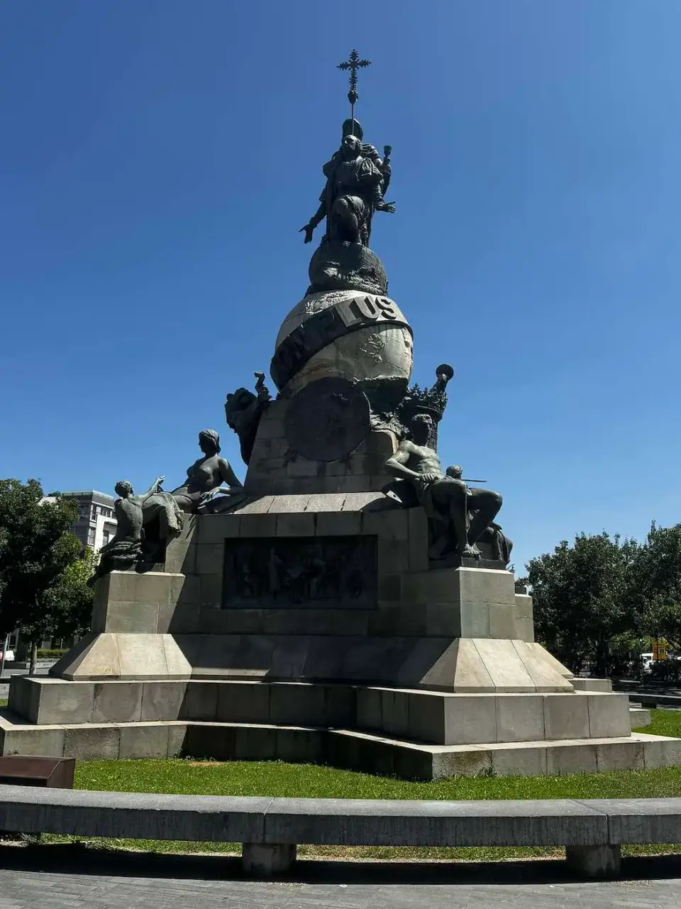 Monumento de bronce y piedra en una plaza ajardinada